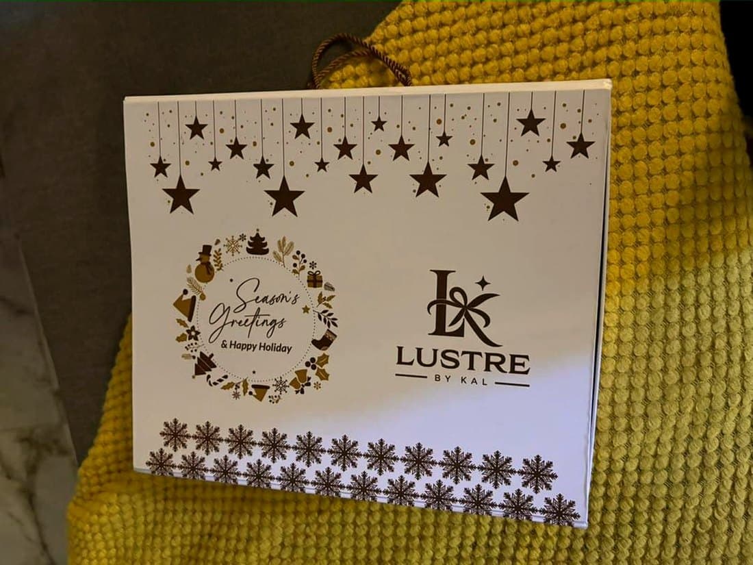 A white Lustre by Kal Season's Greetings gift box with hanging gold stars, a festive wreath and the LK monogram